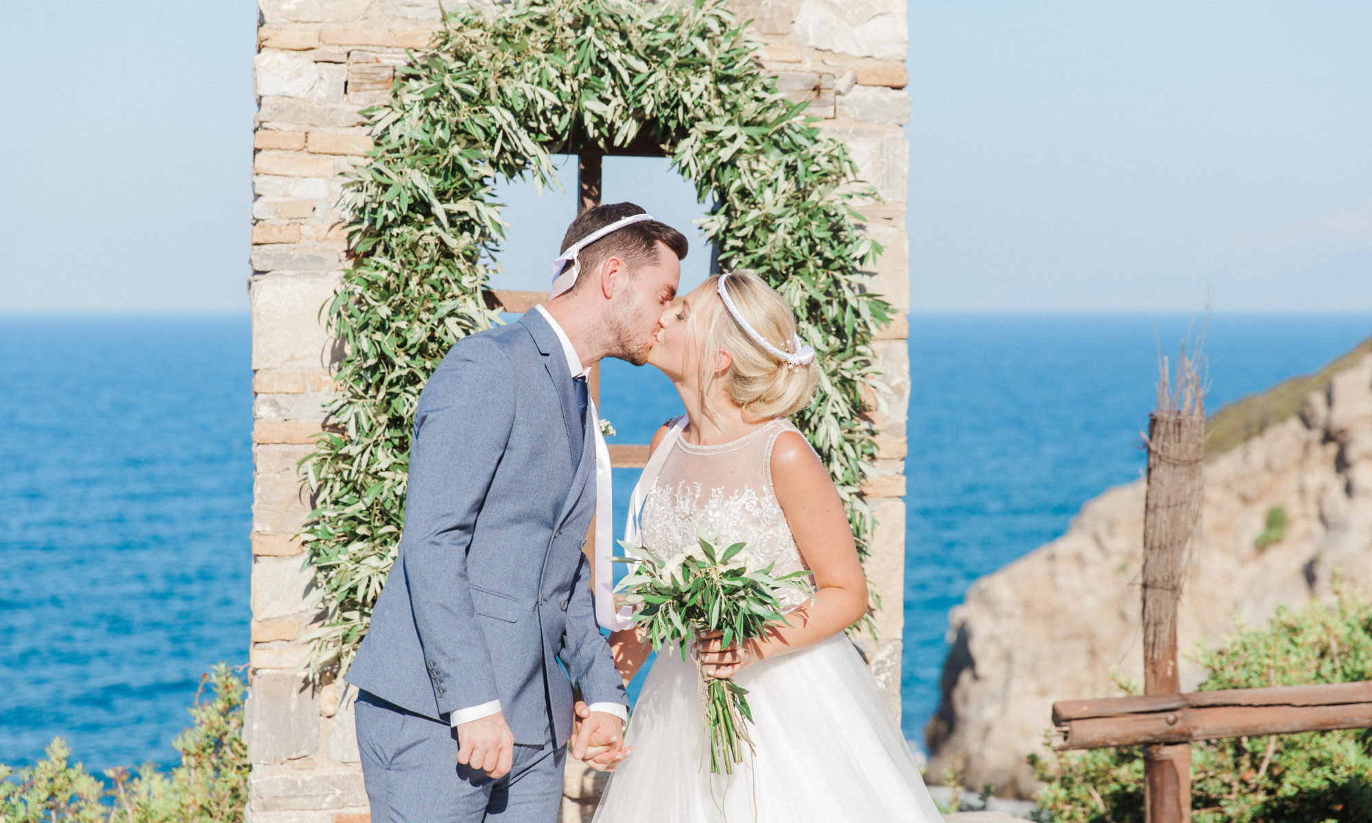 The couples first kiss at the end of their celebrant led wedding ceremony at Villa Delenia in Evia Greece. The couple are wearing Greek wedding crowns.